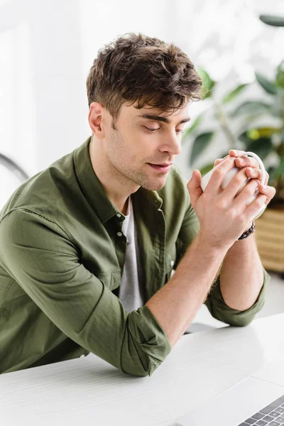 Homem de negócios bonito em camisa verde sentado à mesa com copo no escritório — Fotografia de Stock