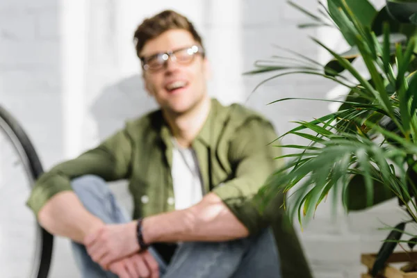 Selective focus of man in green shirt, jeans sitting on floor near brick wall, and plants in office — Stock Photo