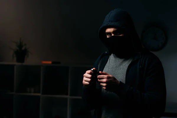 Einbrecher mit Maske steht im dunklen Raum und hält Schlüssel in der Hand — Stockfoto