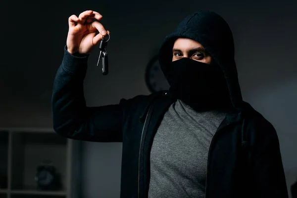 Грабитель в маске и капюшоне держит ключи и смотрит в камеру — стоковое фото