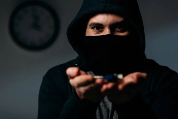 Verbrecher in Kapuzenpulli und Maske zeigt Schlüssel vor Kamera — Stockfoto