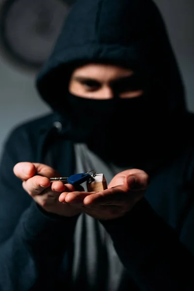 Преступник в черной толстовке и маске показывает ключи перед камерой — стоковое фото