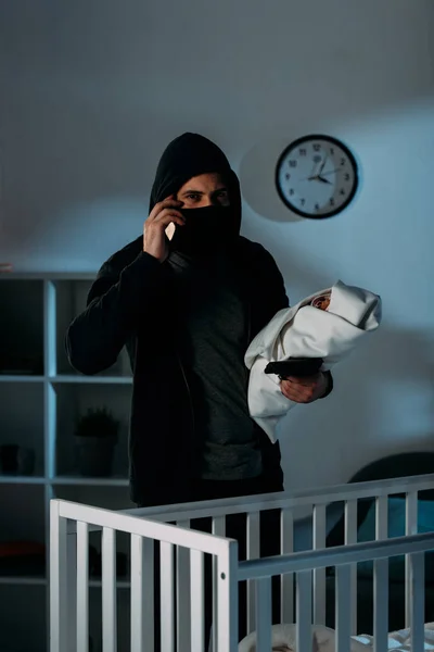 Kidnapper in mask holding infant child and talking on smartphone — Stock Photo