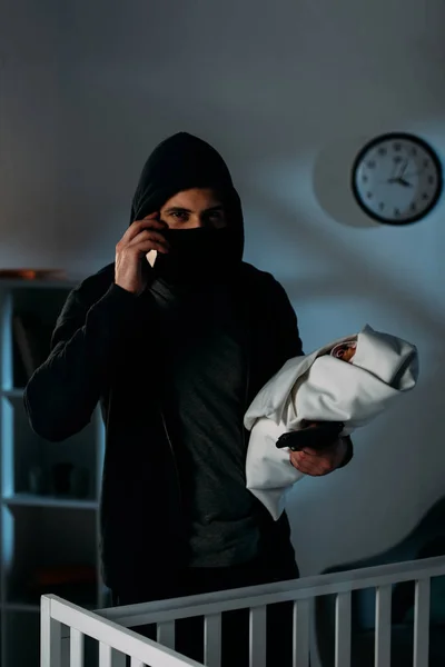 Kidnapper with gun holding infant child and talking on smartphone — Stock Photo