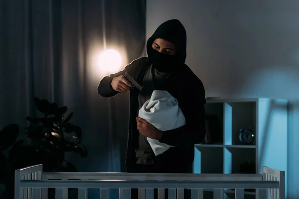 Maskierter Kidnapper zielt im dunklen Raum mit Waffe auf Kleinkind — Stockfoto