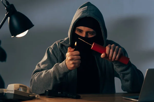 Terrorist in mask and hoodie igniting dynamite in room — Stock Photo