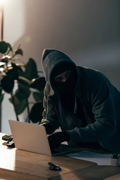 Verbrecher maskiert mit Laptop im dunklen Raum — Stockfoto