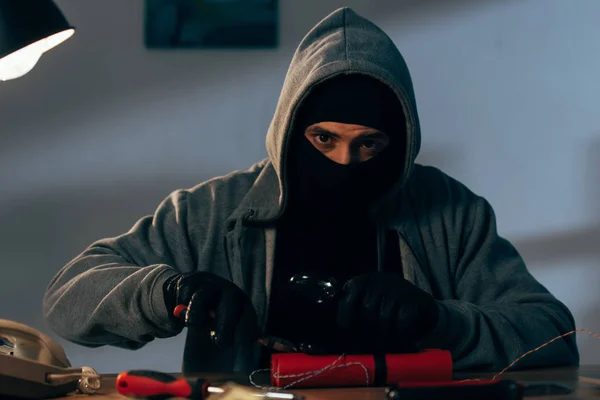 Terrorist in mask and gloves making bomb and looking at camera — Stock Photo