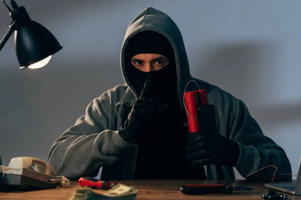 Terrorist in mask holding dynamite and showing hush sign — Stock Photo