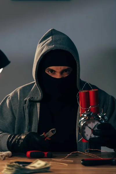 Angry terrorist in mask making bomb and looking at camera — Stock Photo