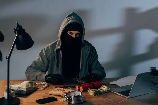 Verbrecher in Maske mit Pistole und Dynamit sitzt am Tisch und schaut in die Kamera — Stockfoto