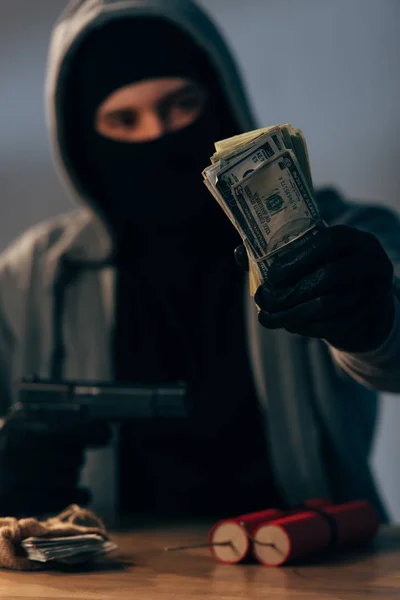 Terrorist in mask and gloves holding gun and dollar banknotes — Stock Photo