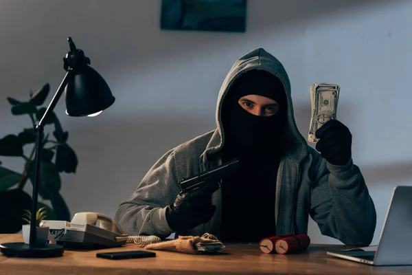 Terrorista en máscara y guantes con pistola y billetes de dólar - foto de stock
