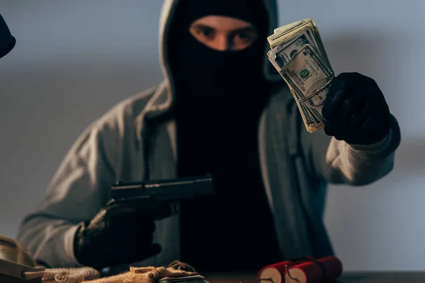 Terrorista en máscara sosteniendo arma y mostrando billetes de dólar - foto de stock