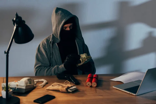 Terrorista sentado en la habitación con arma y contando billetes de dólar - foto de stock