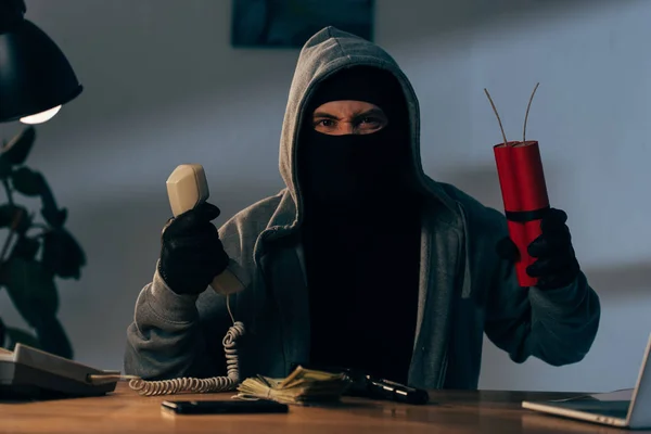 Angry terrorist in mask holding handset and dynamite in room — Stock Photo