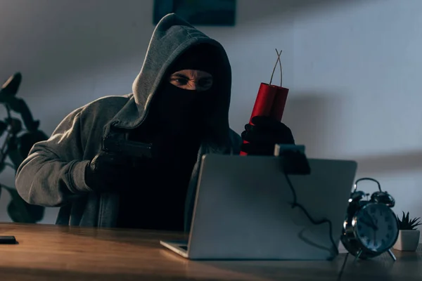 Agresivo terrorista en máscara apuntando arma a webcam en cuarto oscuro - foto de stock