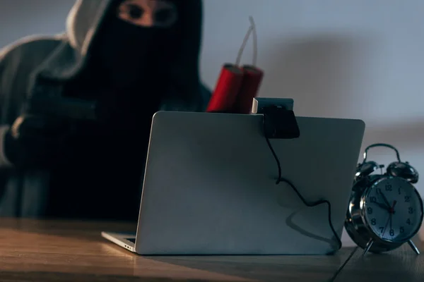 Terrorist in mask holding dynamite while using laptop in dark room — Stock Photo