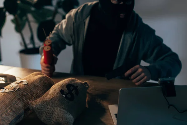 Vista recortada del terrorista con pistola y dinamita sentado a la mesa con bolsas de dinero - foto de stock