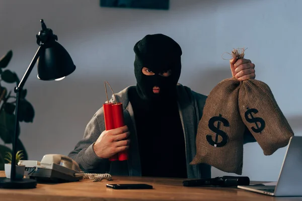 Terrorist in mask holding dynamite and money bags in room — Stock Photo