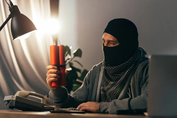 Terrorista en máscara mirando dinamita iluminada en la habitación - foto de stock
