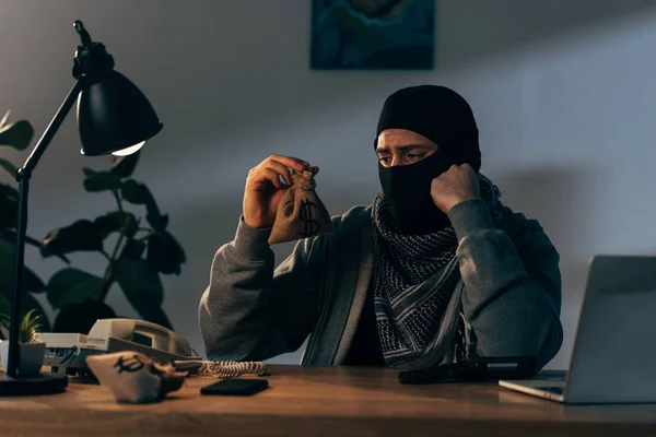 Terrorista perturbado em máscara preta olhando para pequeno saco de dinheiro — Fotografia de Stock
