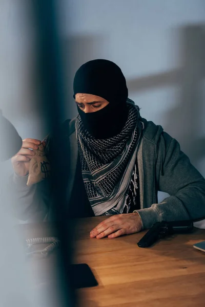 Upset criminal in black mask sitting at table and holding small money bag — Stock Photo