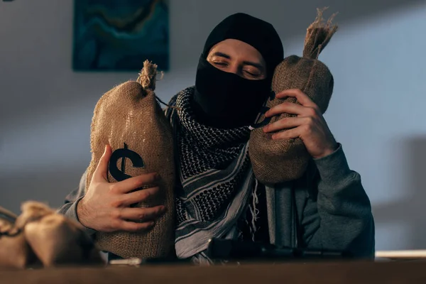 Terrorist in mask holding bags with dollars with closed eyes — Stock Photo