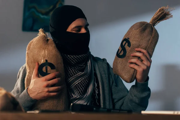 Terrorist in mask holding bags with dollars in room — Stock Photo