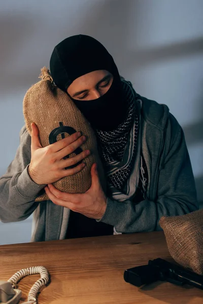 Pleased terrorist in mask embracing money bag with closed eyes — Stock Photo