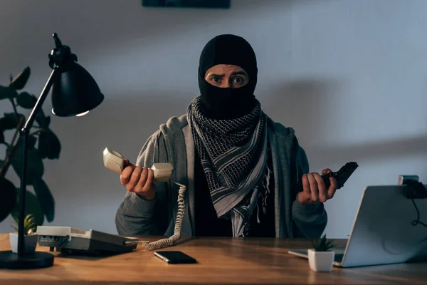 Disappointed terrorist in mask holding gun and telephone handset — Stock Photo