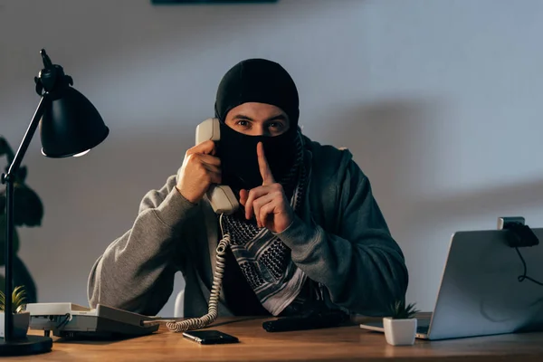 Terrorist in mask talking on telephone and showing hush sign — Stock Photo