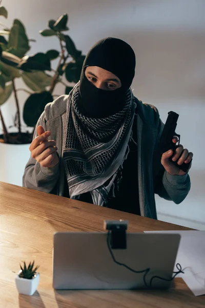 Terrorist in black mask showing gun in video chat in room — Stock Photo