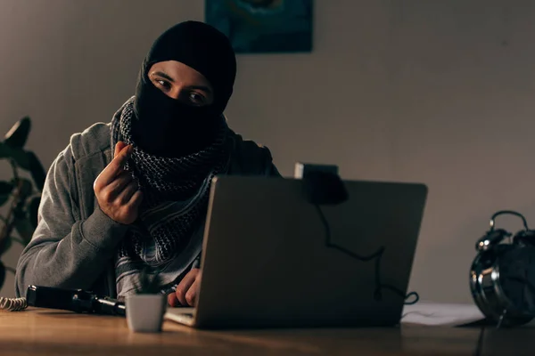 Terrorista en máscara mirando a la webcam y mostrando el gesto de dinero - foto de stock