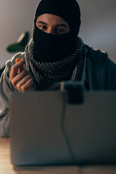 Fröhlicher Terrorist in Maske blickt auf Webcam und zeigt Geld-Geste — Stockfoto