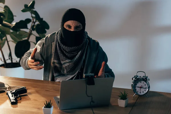 Wütender Terrorist mit schwarzer Maske gestikuliert vor Webcam im Zimmer — Stockfoto