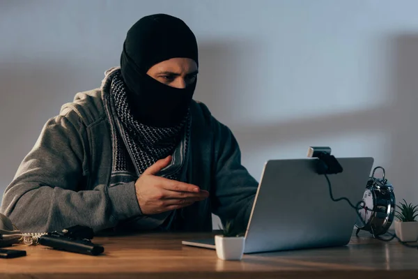Terrorista en máscara negra utilizando el ordenador portátil y mirando a la webcam - foto de stock