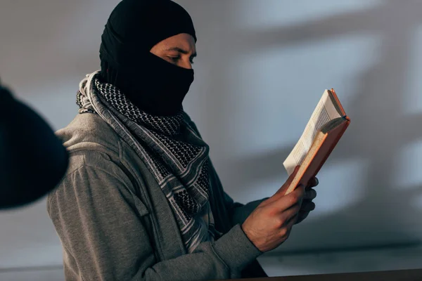 Terrorista en máscara negra y keffiyeh bufanda libro de lectura - foto de stock