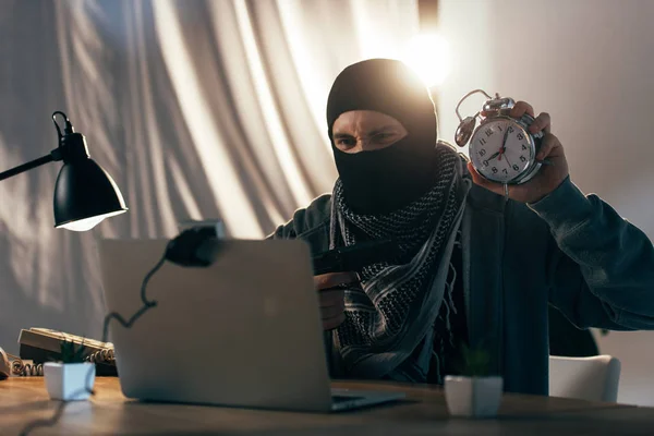 Angry terrorist with gun showing alarm clock at webcam — Stock Photo