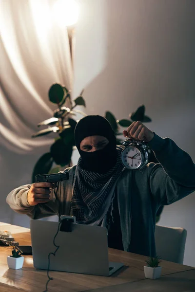 Aggressive terrorist with gun showing alarm clock in video chat — Stock Photo