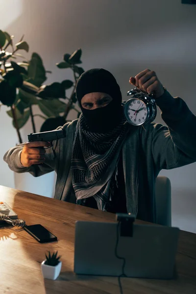 Angry terrorist in mask aiming gun at alarm clock in room — Stock Photo