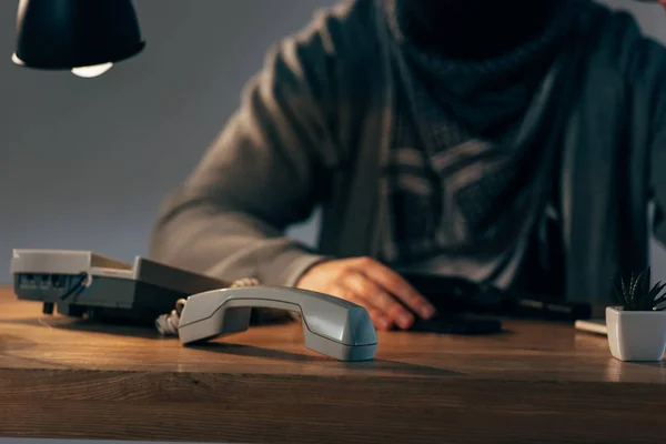 Обрізаний вид терориста, що сидить за столом з телефоном — стокове фото