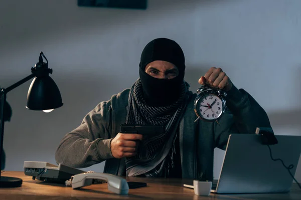 Aggressive terrorist holding gun and alarm clock and looking at camera — Stock Photo