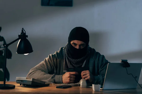Aggressiver Terrorist sitzt mit Waffe am Tisch und blickt in Kamera — Stockfoto