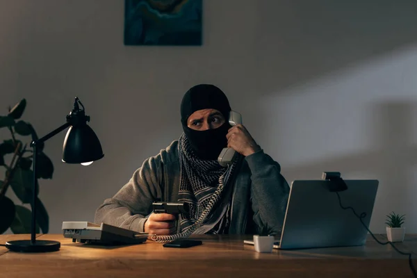 Terroriste inquiet masqué parlant au téléphone et tenant une arme — Photo de stock