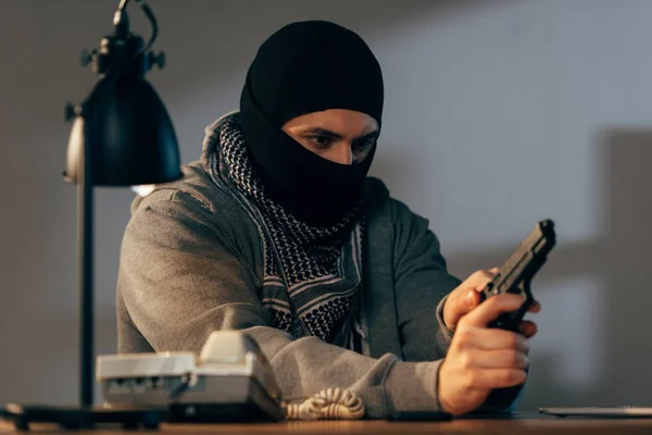 Concentrated criminal in black mask loading gun in room — Stock Photo