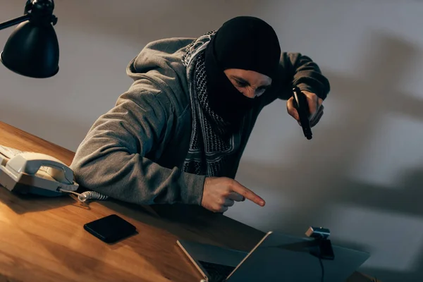 Angry terrorist pointing with finger and aiming gun at laptop screen — Stock Photo