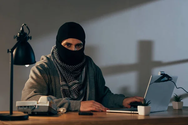 Terrorist in mask and keffiyeh scarf using laptop in room — Stock Photo