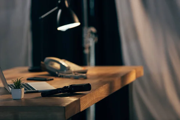 Ordinateur portable, plante verte et pistolet sur une table en bois dans une pièce sombre — Photo de stock