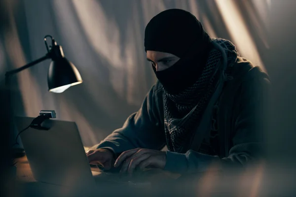 Terrorist in black mask typing on laptop keyboard in room — Stock Photo